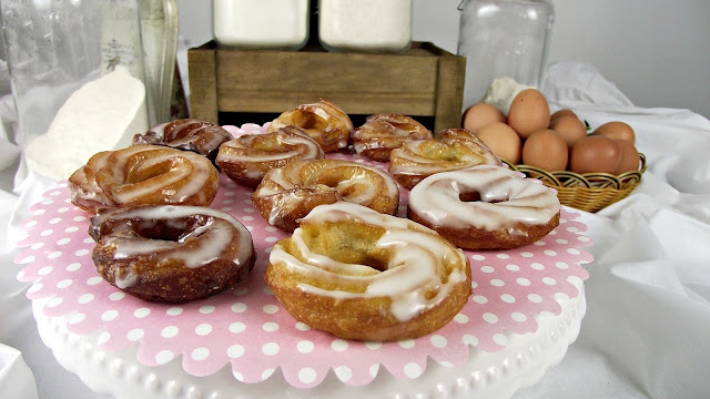 Pasteles glaseados con remolinos blancos sobre un soporte de lunares rosas, rodeados de tarros de harina y huevos, atmósfera de cocina rústica y acogedora