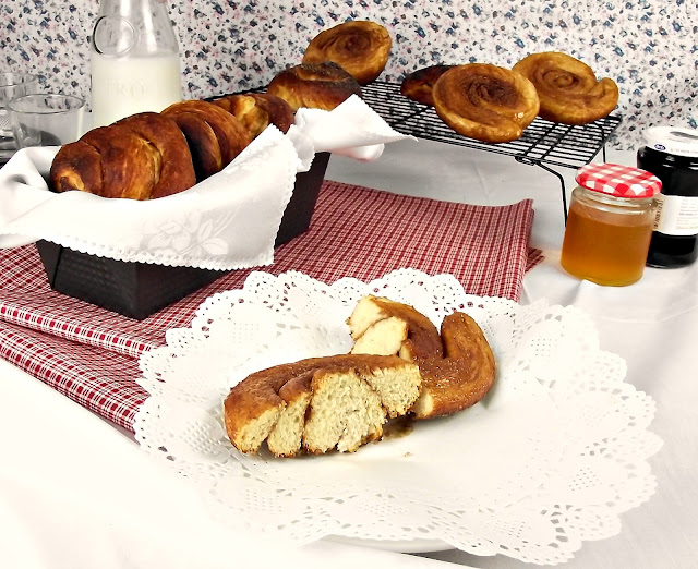Cesta de croissants dorados y bollería con tarros de mermelada sobre un paño de encaje, ambiente cálido de panadería