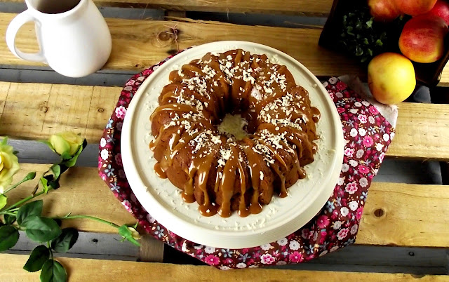 Vista cenital de un bundt cake bañado generosamente en salsa de caramelo y cubierto de coco rallado, sobre una superficie clara