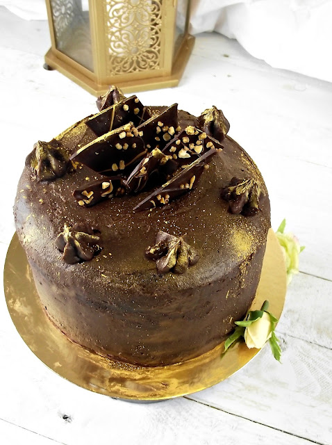 Pastel redondo de chocolate cubierto con virutas de chocolate y acentos dorados, tonos marrones y dorados, ambiente elegante