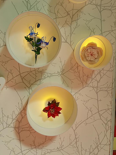Luces redondas de pared con flores decorativas en su interior, sobre papel pintado con motivos de ramas, luz cálida y ambiente acogedor