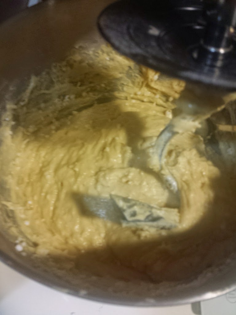 Masa espesa de color amarillo en un bol metálico de batidora, con el accesorio de mezclado visible, ambiente de cocina casera