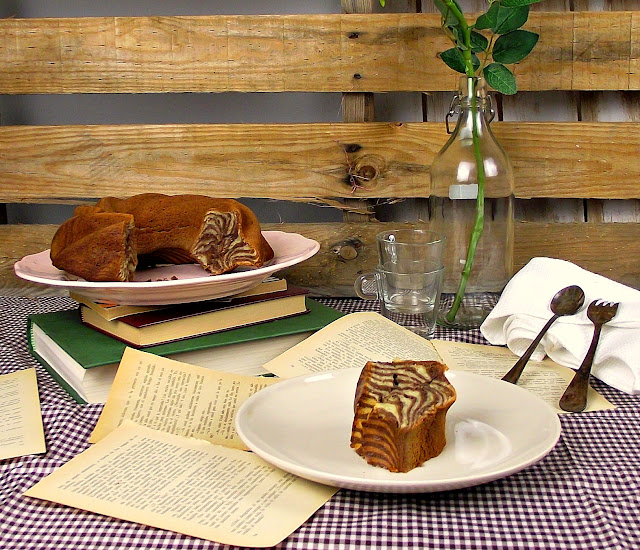 Tarta marmolada en porciones sobre platos junto a páginas de un libro abierto y un jarrón con ramas verdes, ambiente rústico y cálido