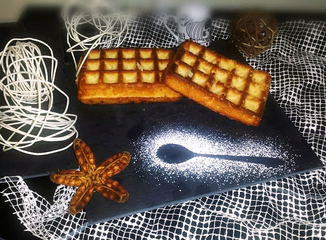 Dos gofres dorados sobre pizarra oscura con azúcar glas y red decorativa, ambiente cálido de postre